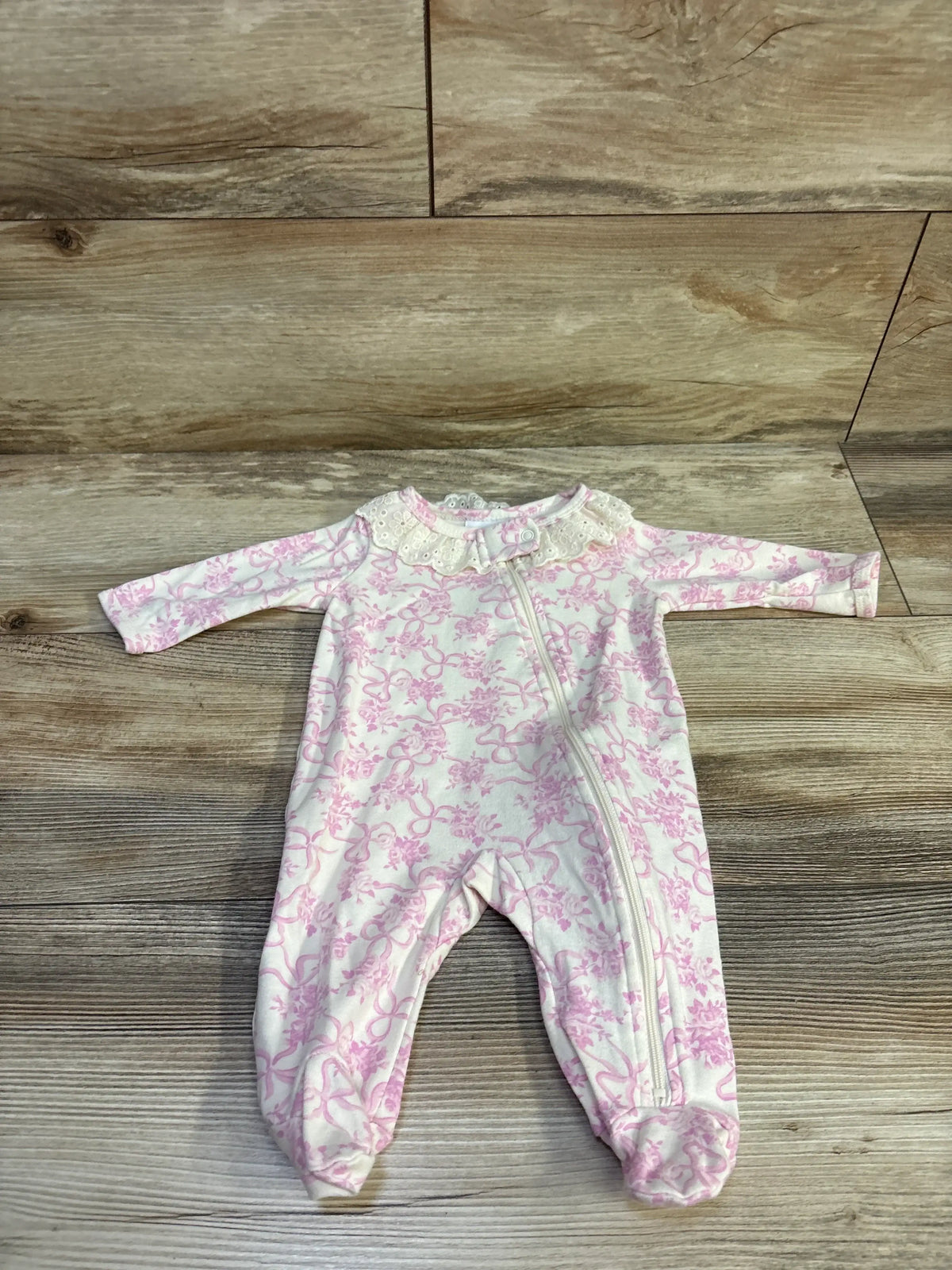 Flat lay of eyelet collar sleeper 0-3M showing lace collar and diagonal zipper, white with pink floral print on wood