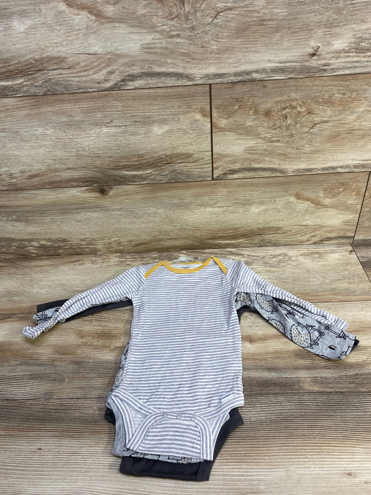 Stack of gently used baby bodysuits, striped and patterned, long sleeve, on wood floor