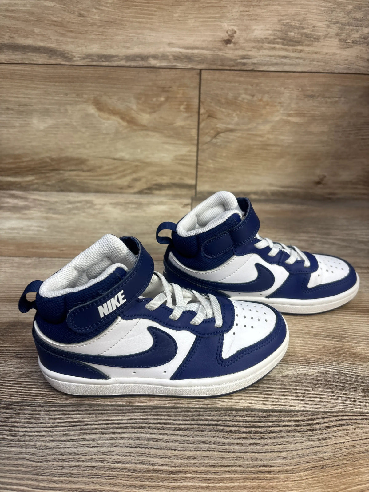 Front three-quarter view of Nike Court Borough Mid 2 TD sneakers in white and Signal Blue on a wood-grain surface