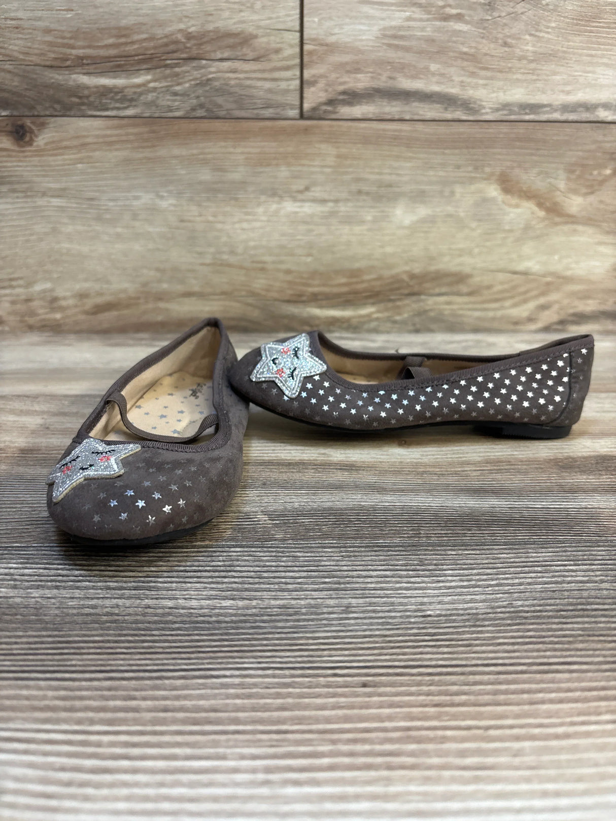 Brown girls' flats with silver star patterns and sequin star accents on wooden floor