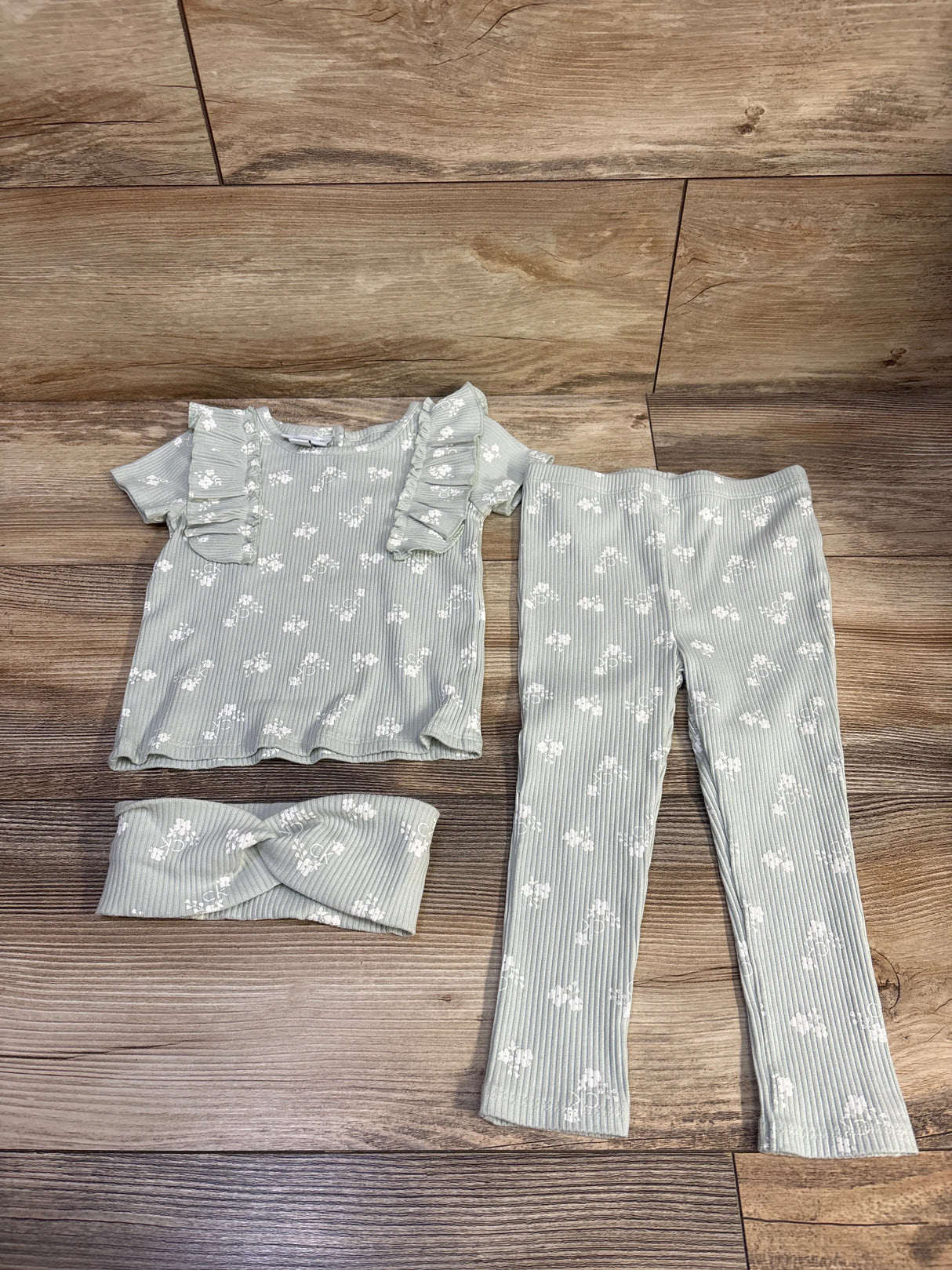 Flat lay of Calvin Klein 3-piece ribbed mint green set with top that has ruffle sleeves, leggings, and headband on wood floor