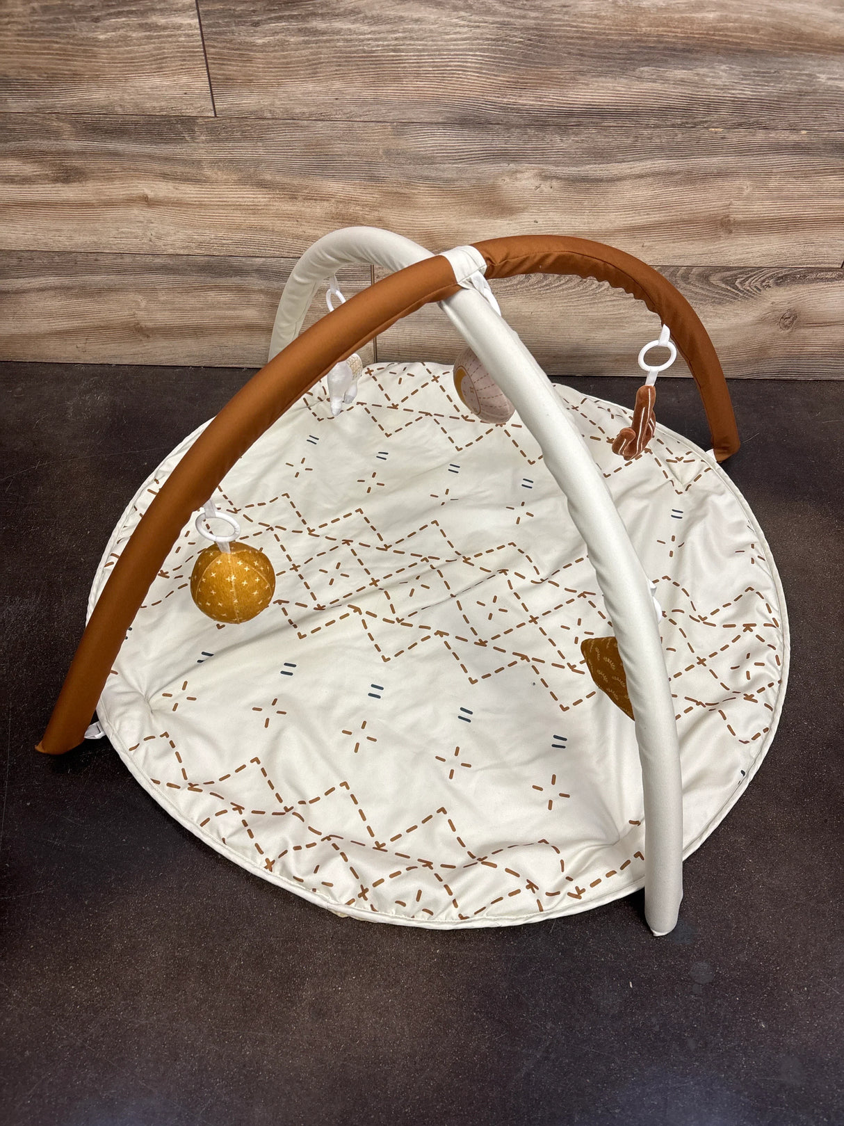 Baby play gym with soft mat, hanging toys, and wooden arches on brown background