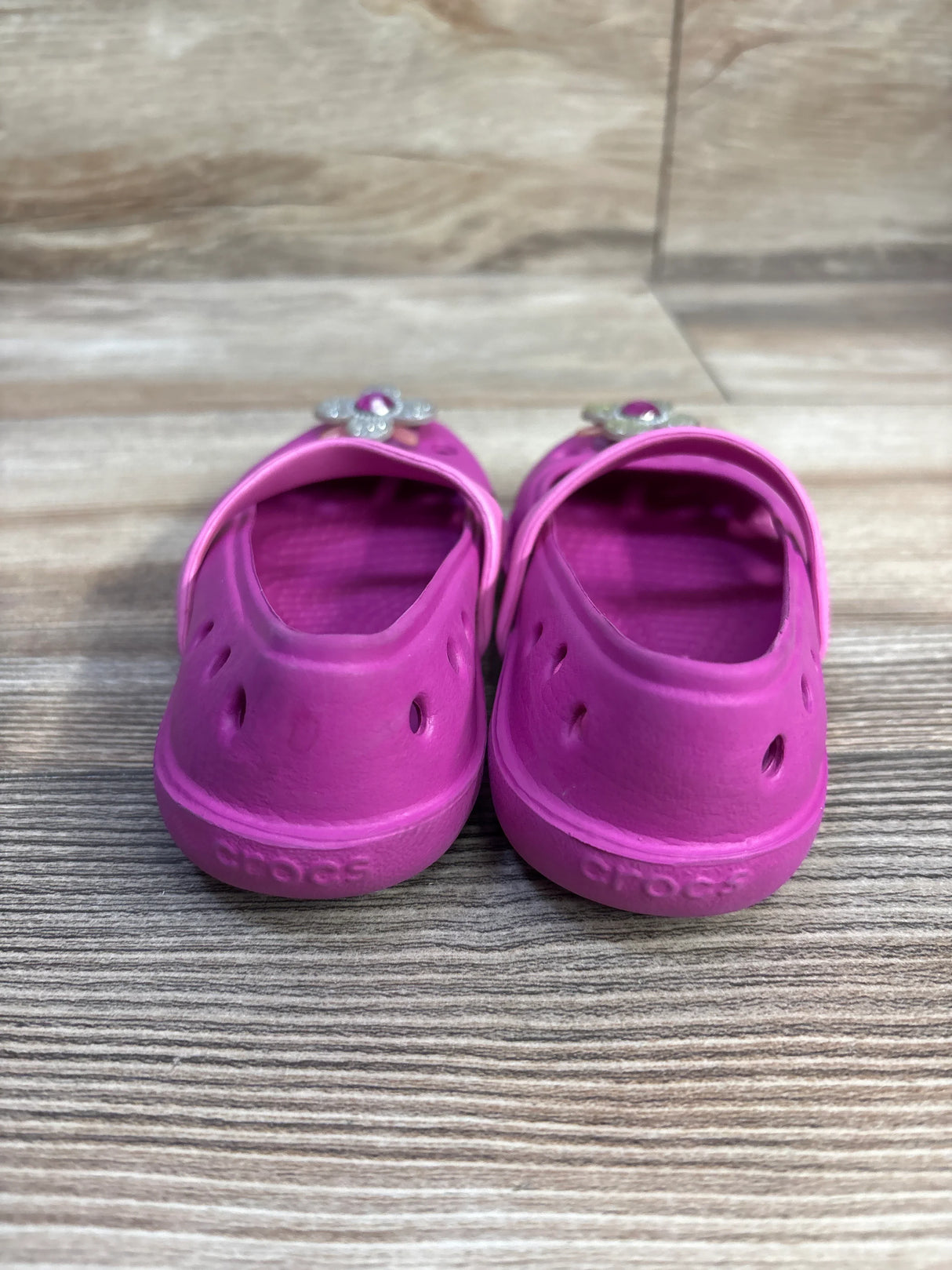 Rear view of Crocs Keeley Petal Charm flats in pink showing flower charm on slingback strap and textured footbed on wood surface