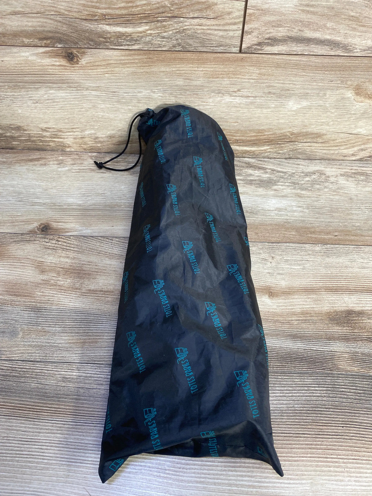 Top-down view of Totes Babies shopping cart car seat hammock folded in black drawstring storage bag on wood floor