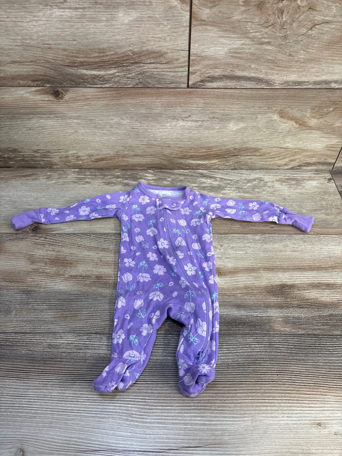 Front view of Member’s Mark newborn floral sleeper showcasing a purple floral print and long sleeves on a wood-look background