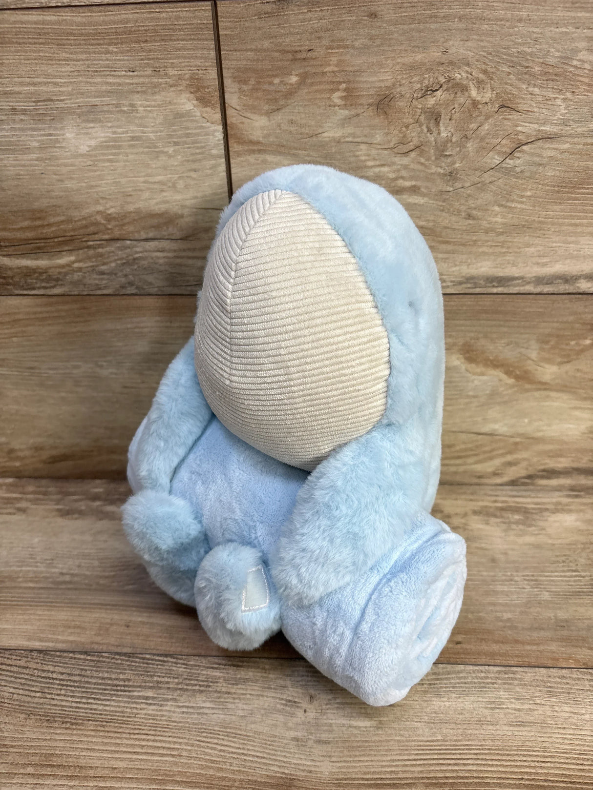 Angled view of Cloud Island blue plush blanket with attached whale toy showing soft fur and beige face on wood backdrop