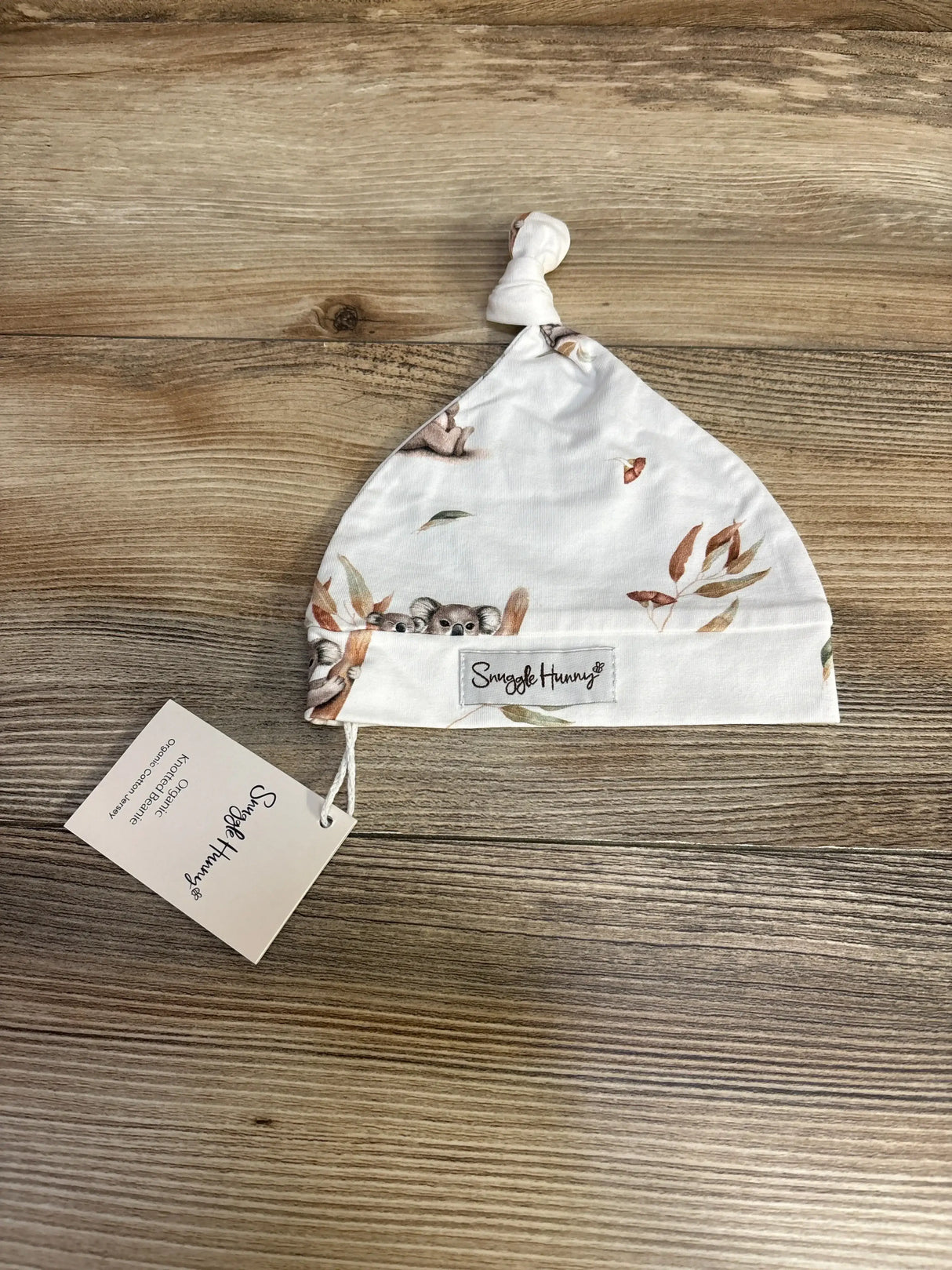 Flat lay of Snuggle Hunny koala organic knotted beanie showcasing knotted top, koala print and brand label on wood surface