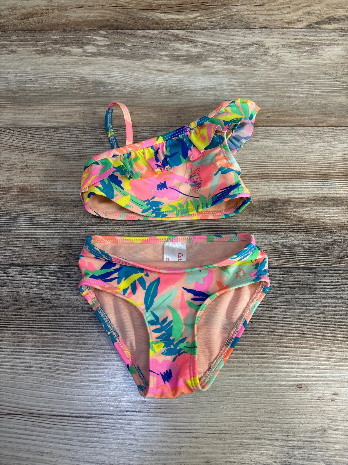 Front view of Cat & Jack peach two-piece swimsuit set with ruffled top and matching bottoms on a wood-grain background