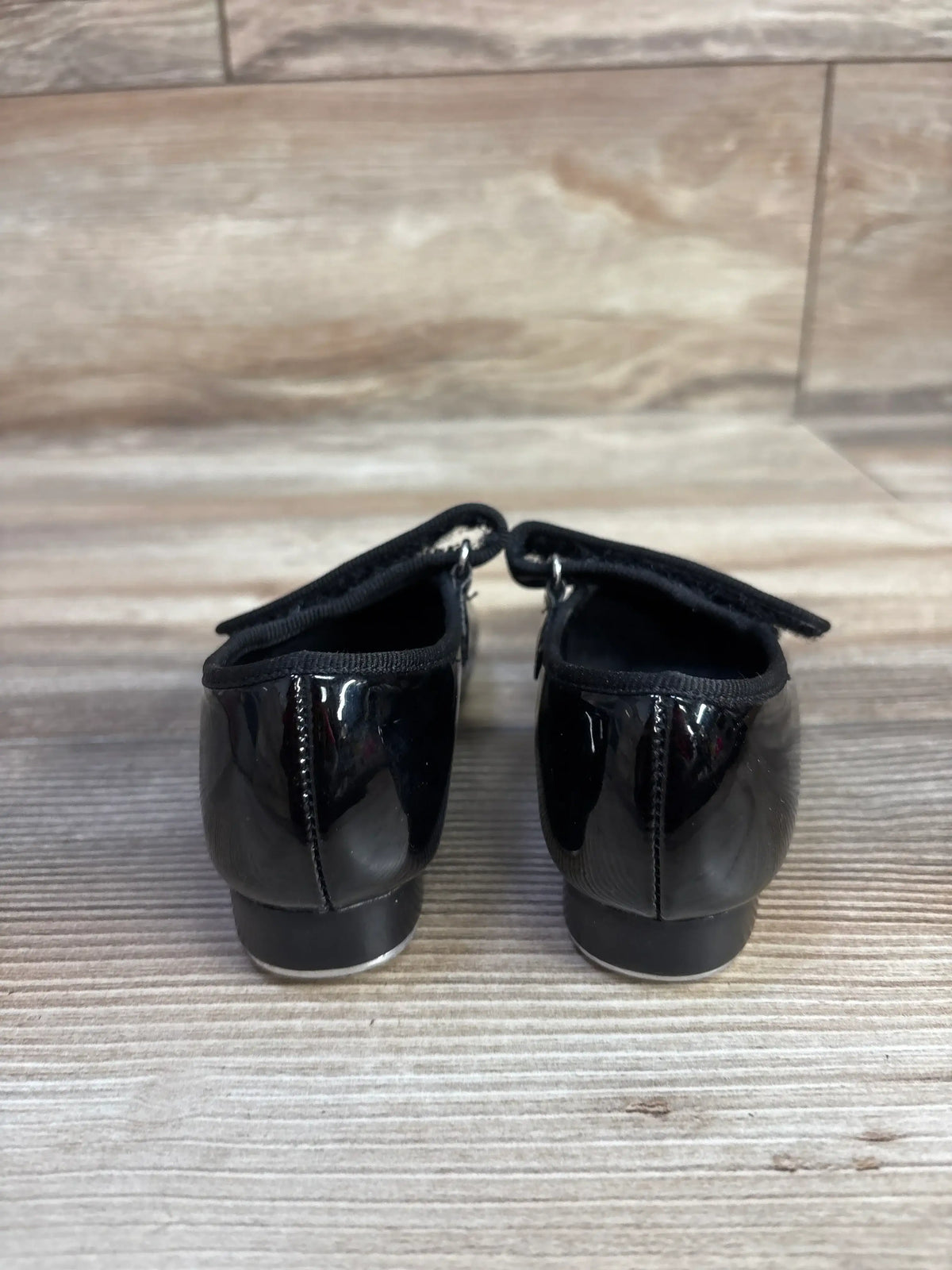 Rear view of black tap shoes in size 7.5c showcasing glossy uppers and heel tap plates on a wood floor