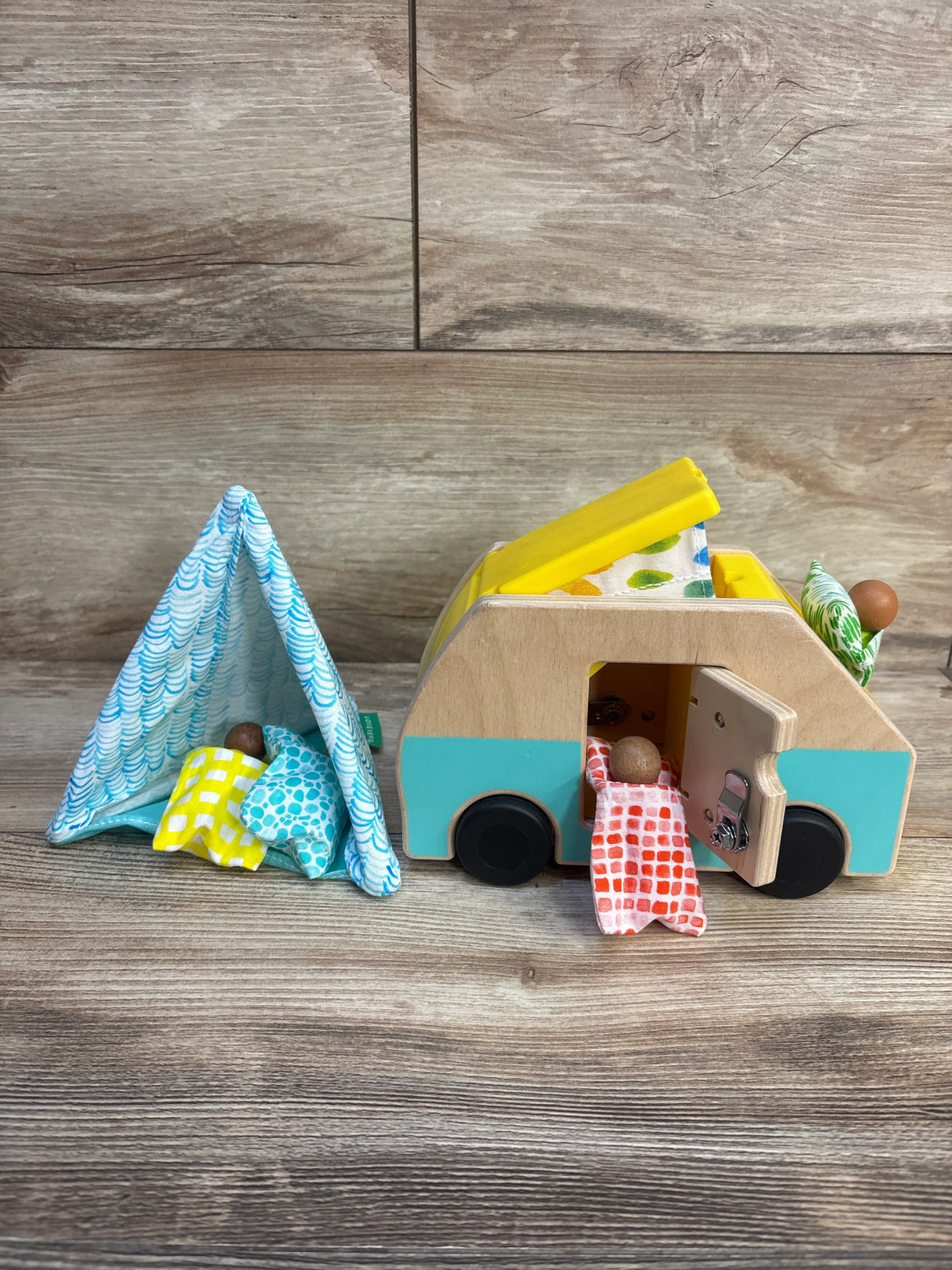 Wooden toy camper set with fabric tent, miniature dolls, and colorful bedding