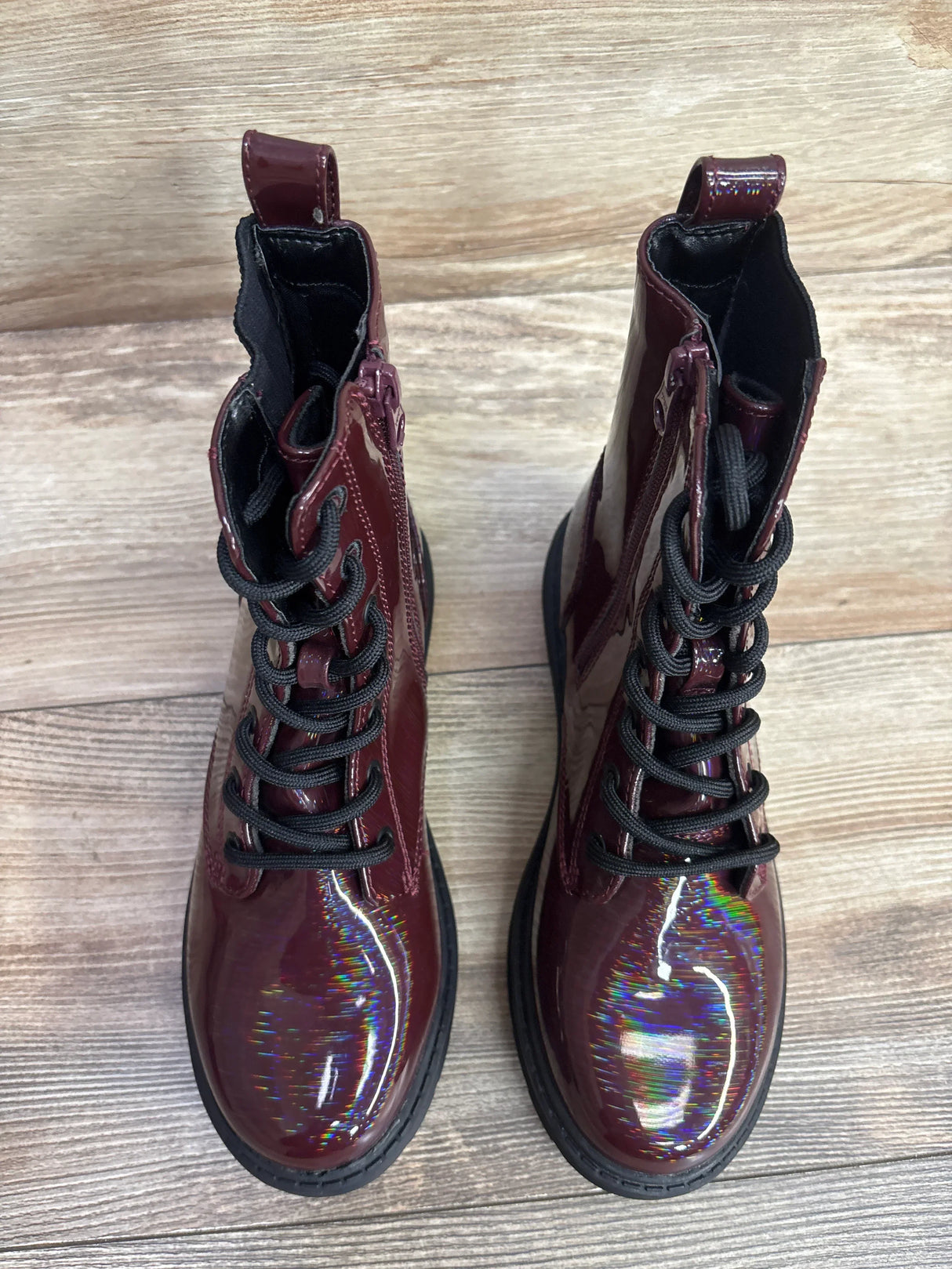 Kids burgundy patent leather combat boots with black laces on wood floor