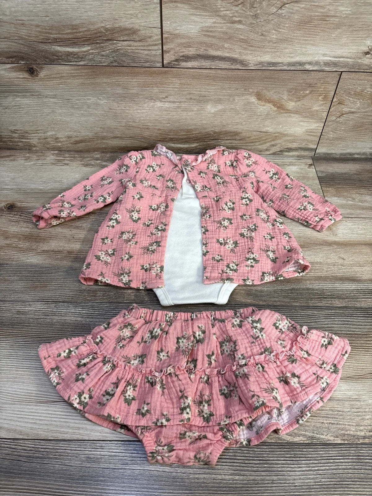 Front view of pink floral two piece bodysuit and bloomers with long sleeves and ruffled bloomers on a wood look floor