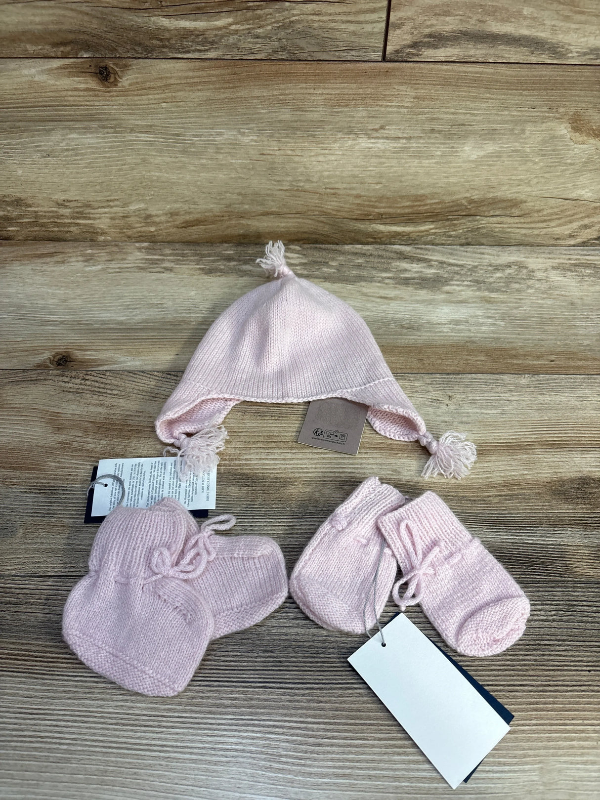 Pink baby knit hat and booties set on wooden background with product tags