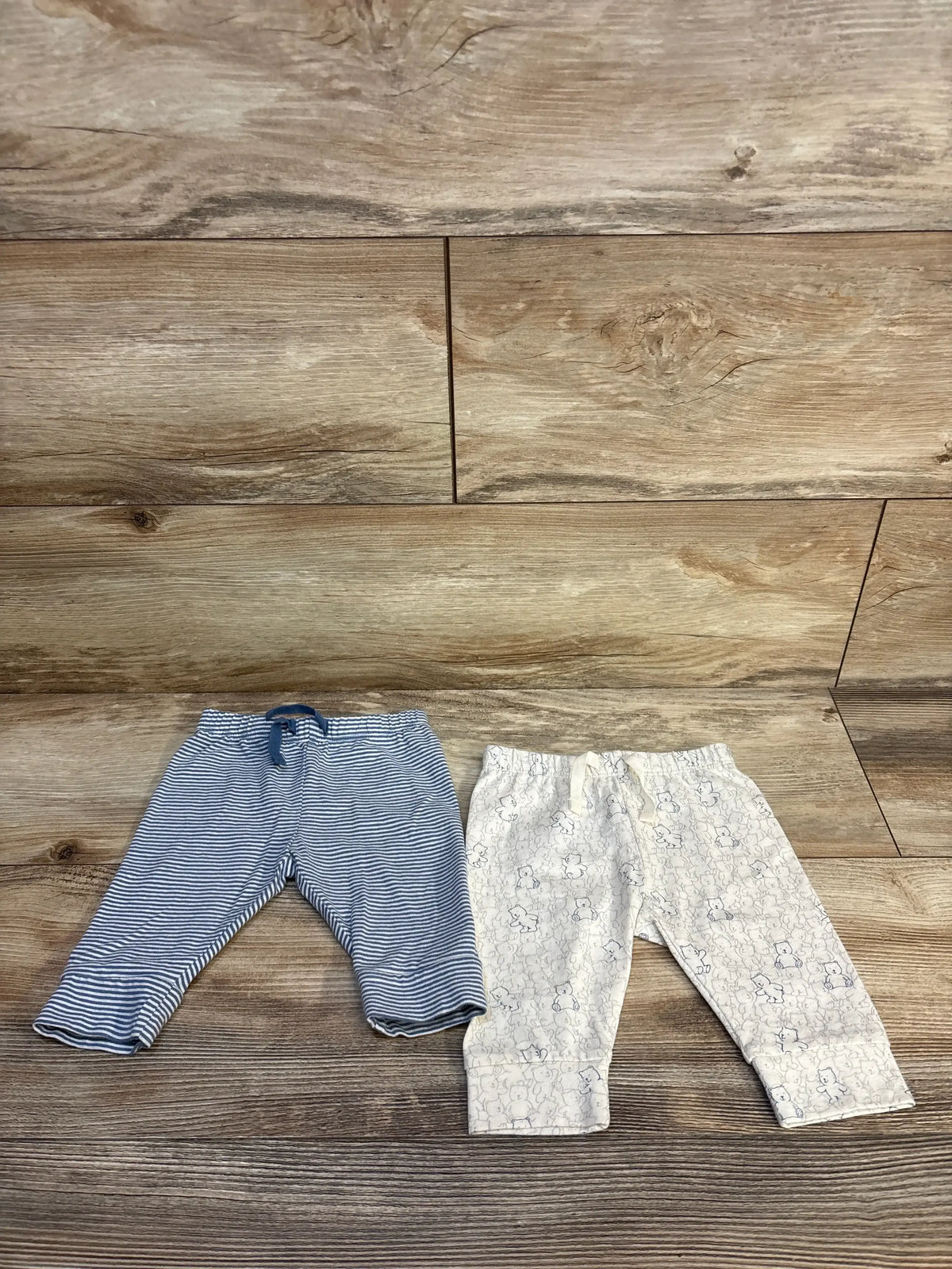 Two pairs of baby pants, one blue striped and one with bear pattern, on wooden floor