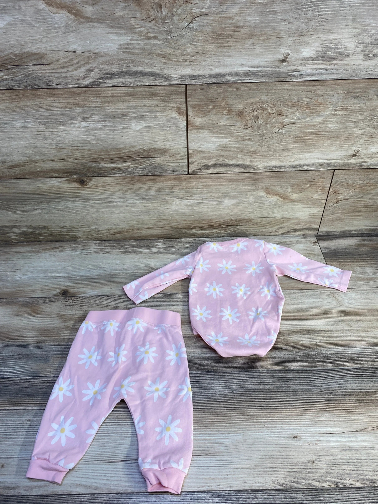 Flat lay of pink 2-piece baby bodysuit and pants set showing white daisy print and cuffed ankles on wood background
