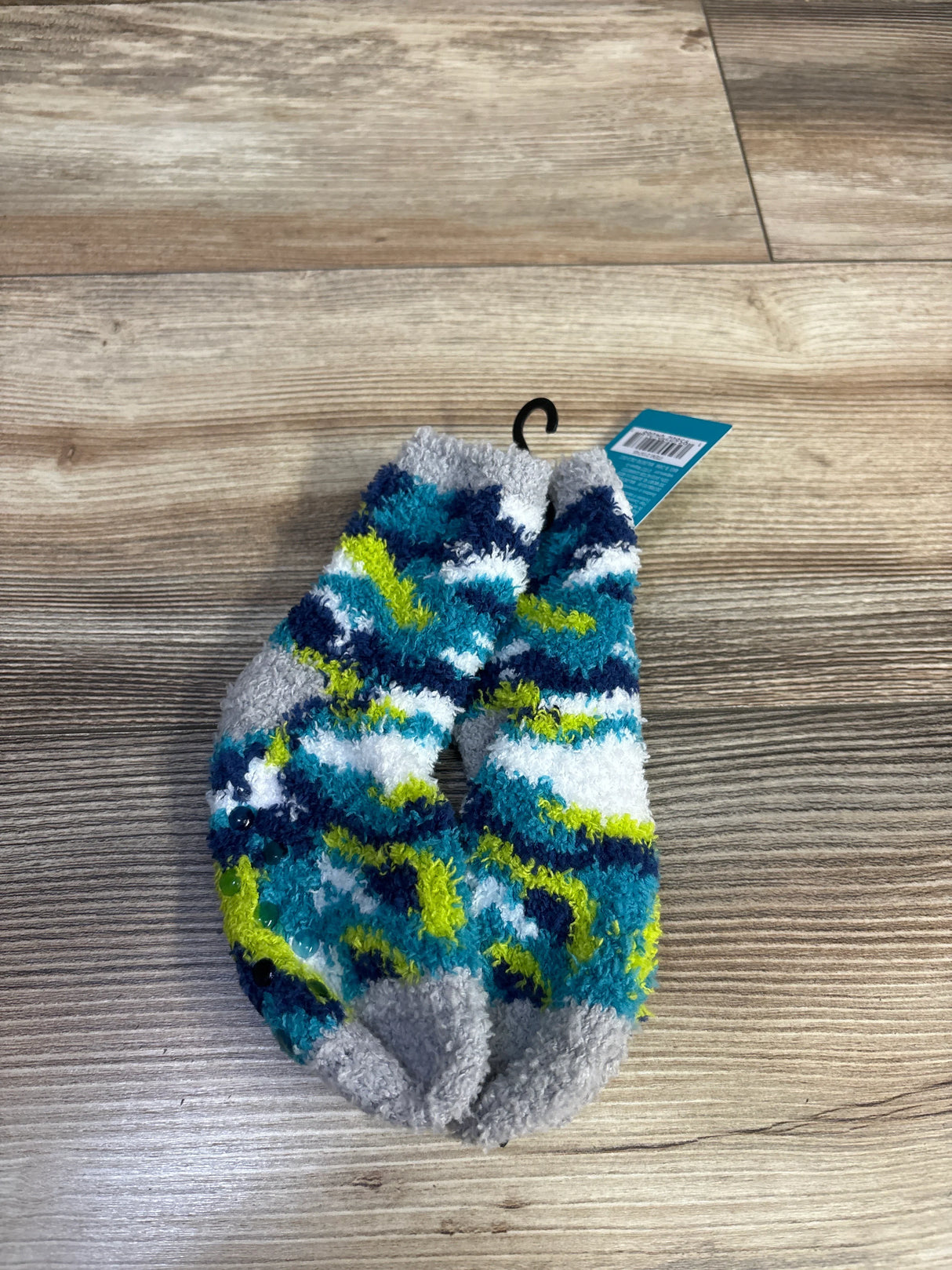 Flat lay of West Loop kids fuzzy socks showing blue, teal, white, and lime stripes and gripper dots on a wood background