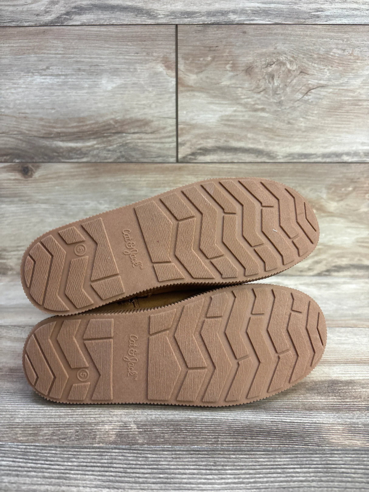 Pair of kid’s shoes with textured rubber soles on wood floor, outsoles facing up