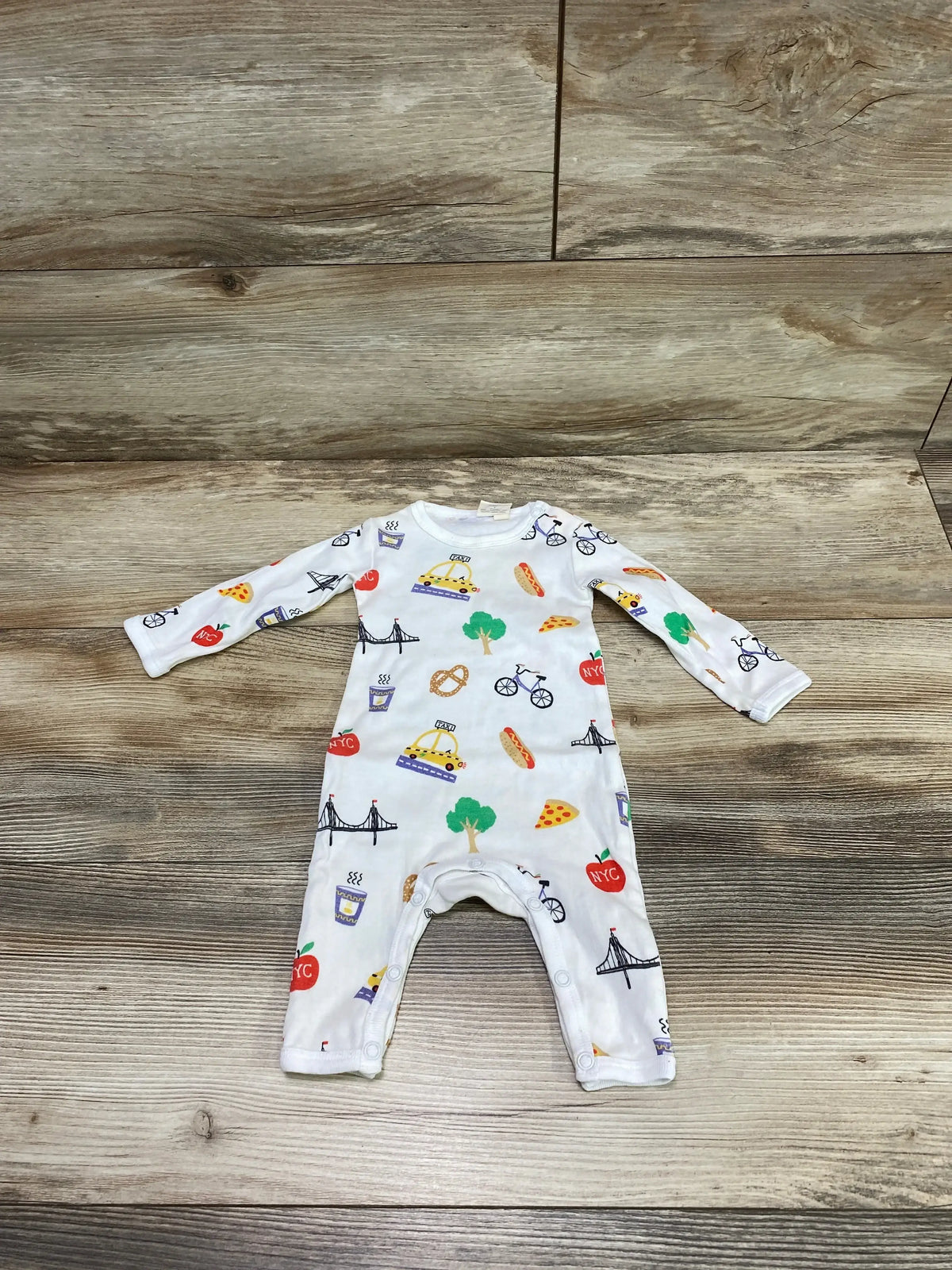 Flat lay of Estalla Organic New York romper onesie showing taxi, pizza, pretzel and NYC apple print on wood background