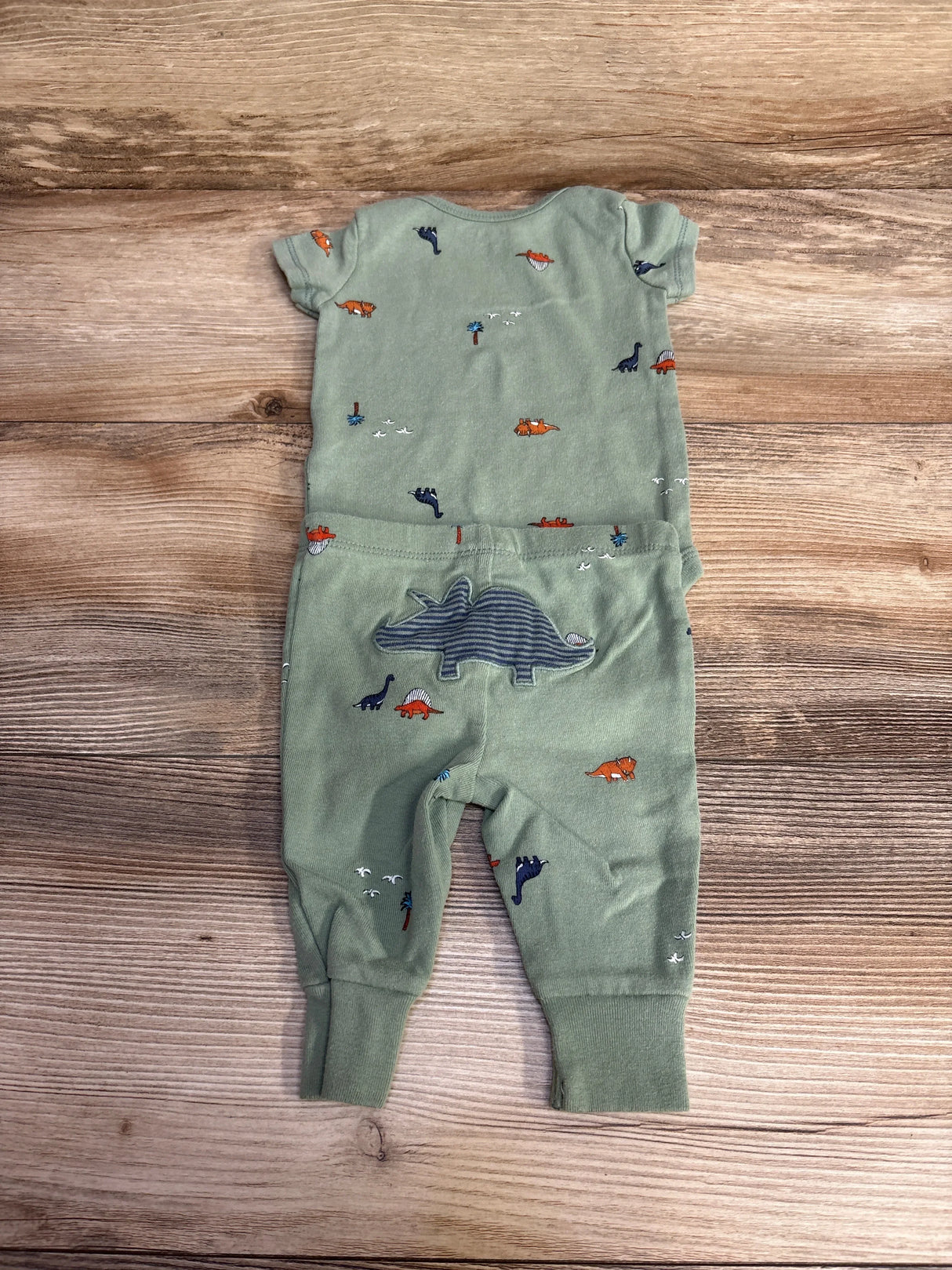 Back view of green Carter's 2pc dinosaur bodysuit and pants with striped dino applique on seat, laid flat on wood
