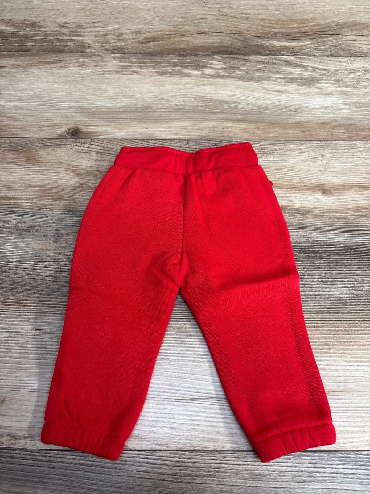 Children's bright red fleece sweatpants with elastic waistband and cuffs on wooden floor