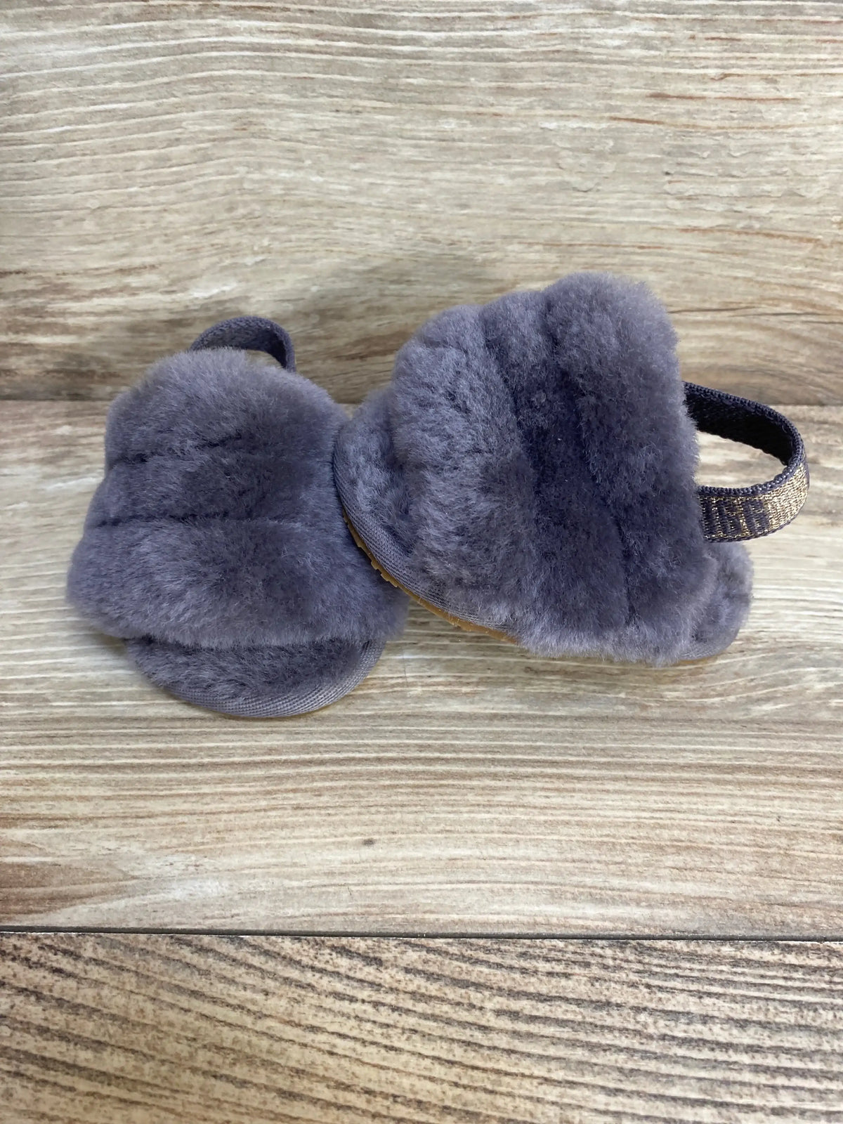 Side and top view of UGG Fluff Yeah toddler slides, grey fluffy sheepskin upper and elastic heel strap on wooden background