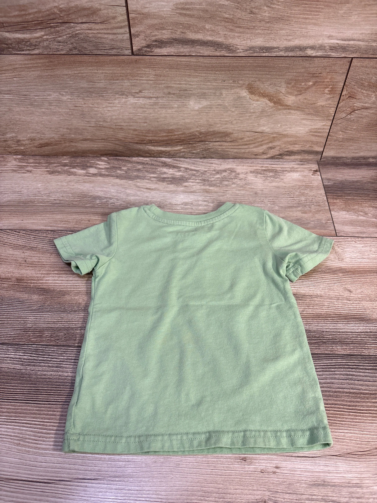 Back view of green toddler T-shirt showcasing plain back and short sleeves with wood floor background
