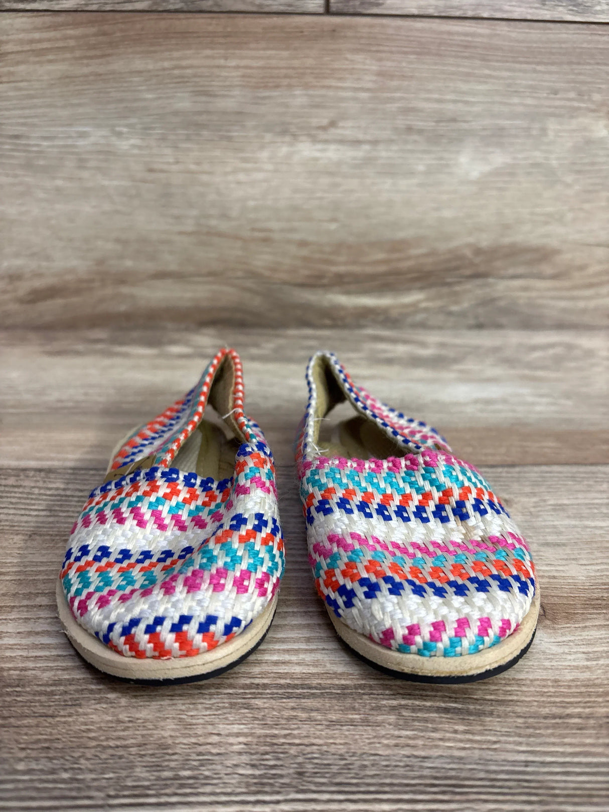 Colorful woven children's slip-on shoes with orange, blue, pink, and turquoise patterns on wood surface