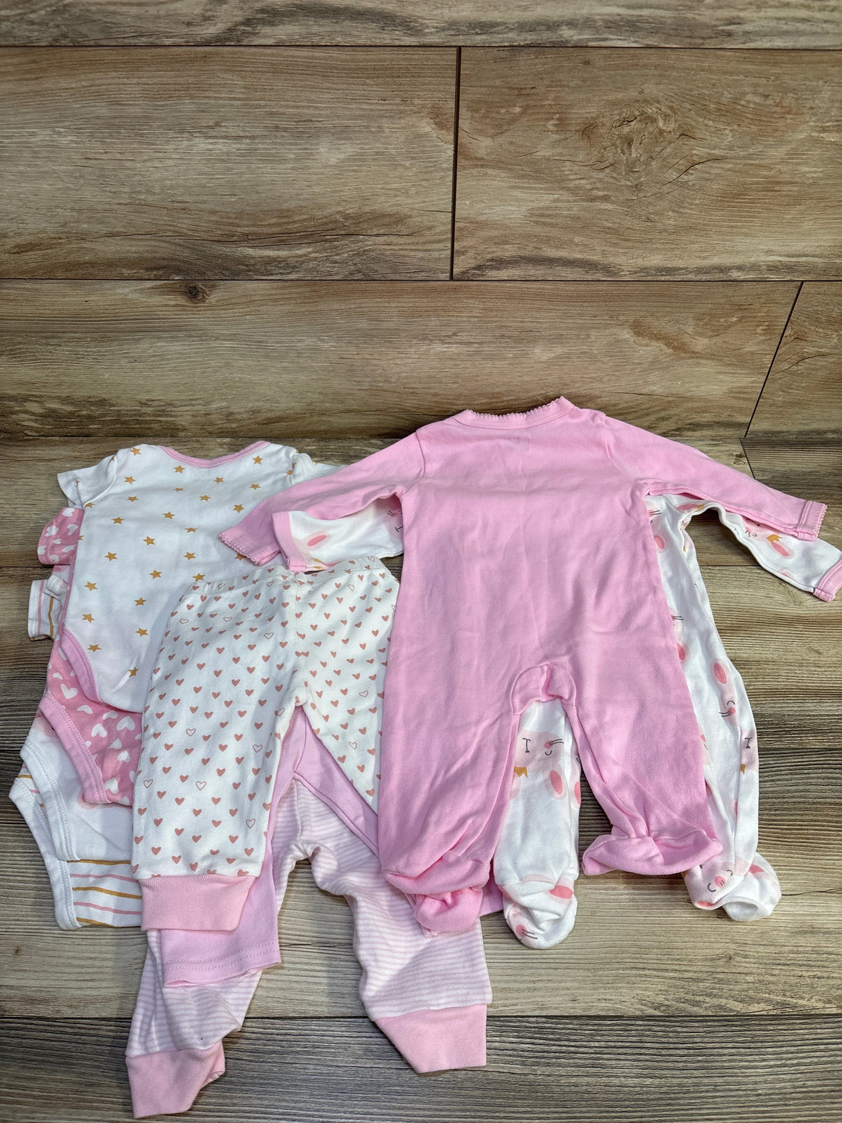 Top-down view of Makimama 9-piece layette set size 6 months showcasing pink and white sleepers, bodysuits, and pants on wood floor background