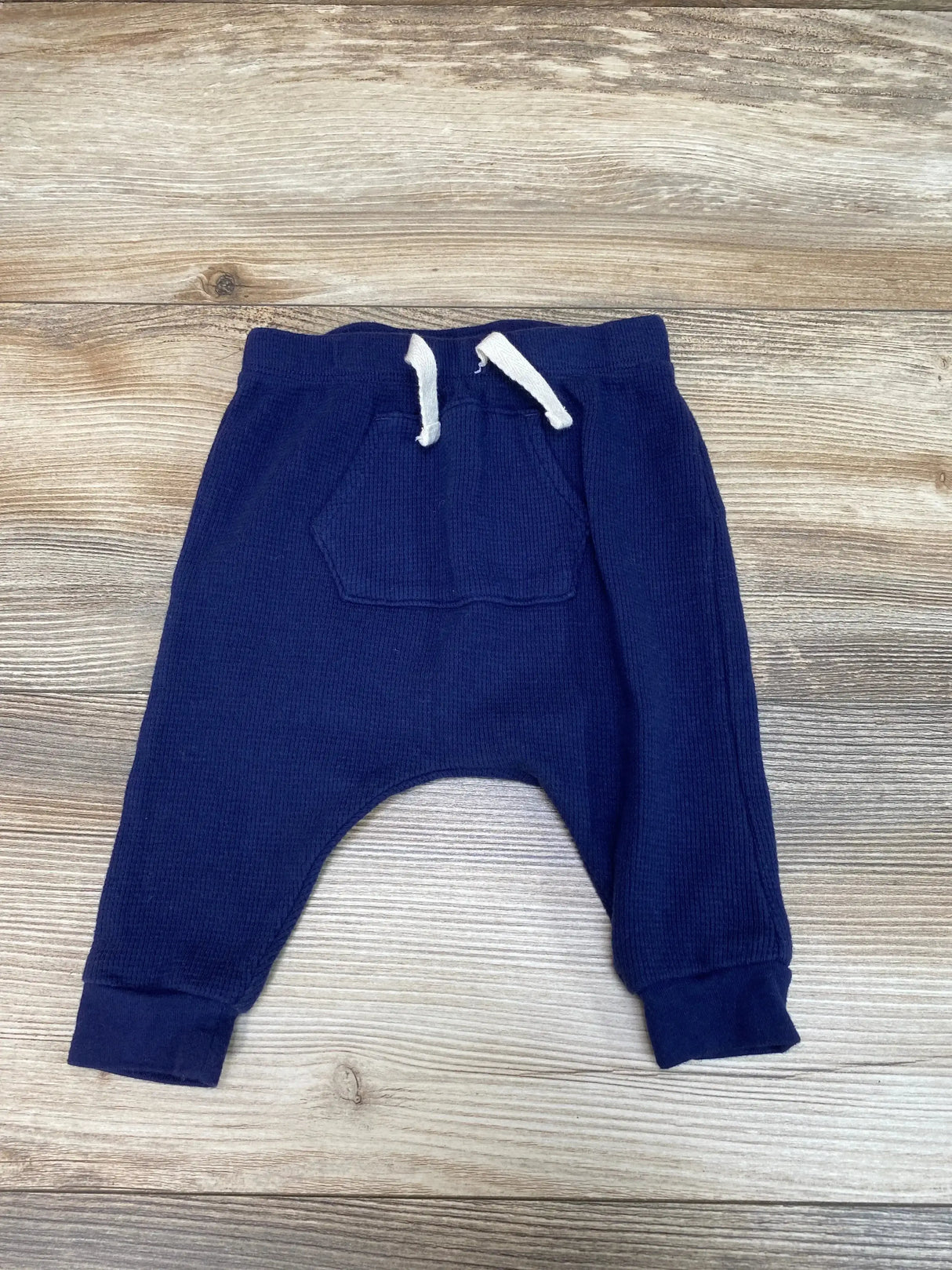 Flat lay of Old Navy navy thermal harem pants 3-6M showcasing waffle knit texture, front pocket, and drawstring on wood background