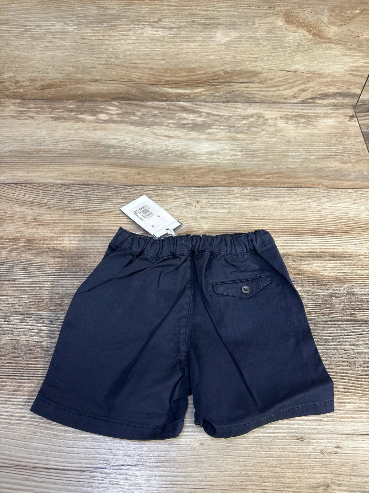 Rear view of navy toddler chino shorts size 12M showing elastic waistband and buttoned back pocket on wood background