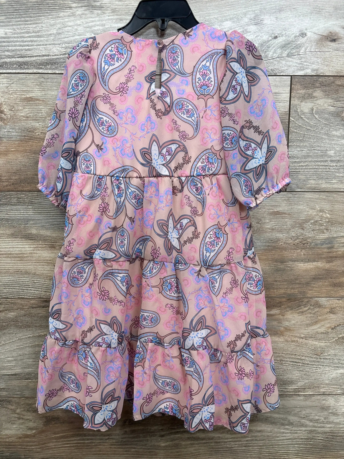 Front view of dusty rose kids' paisley tiered dress showing puff sleeves and three-tier ruffle on a black hanger against wood background
