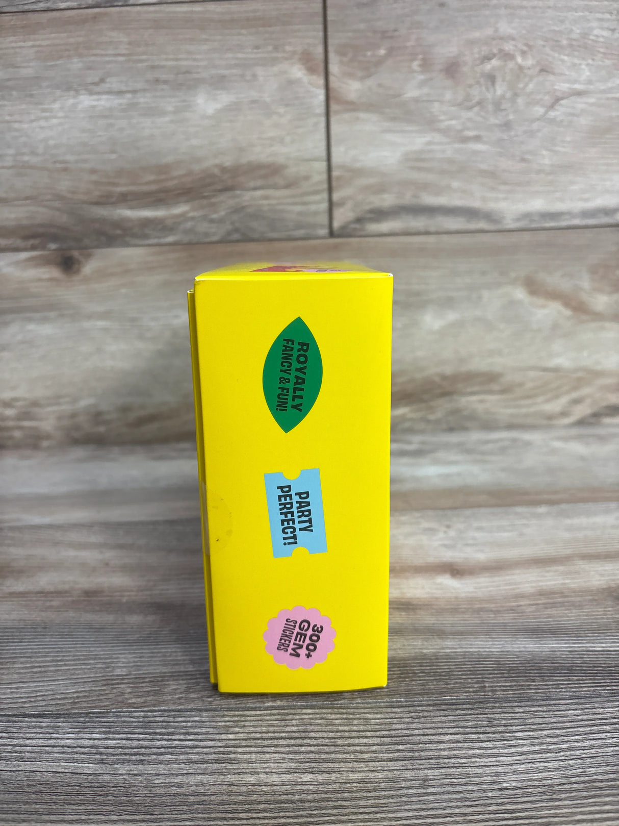 Yellow box with colorful stickers on wooden floor, text includes '300+ gem stickers', 'party perfect', and 'royally fancy & fun'.