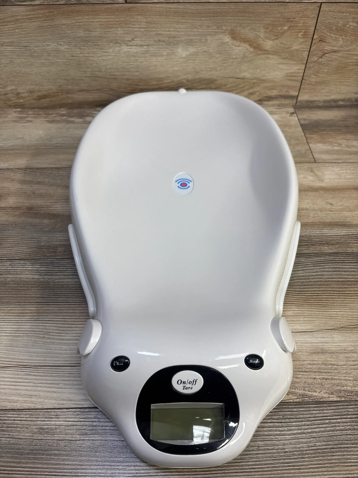 Top view of Baby Doppler MiniMax Digital Baby Scale showcasing white infant tray and digital display on a wood-look floor