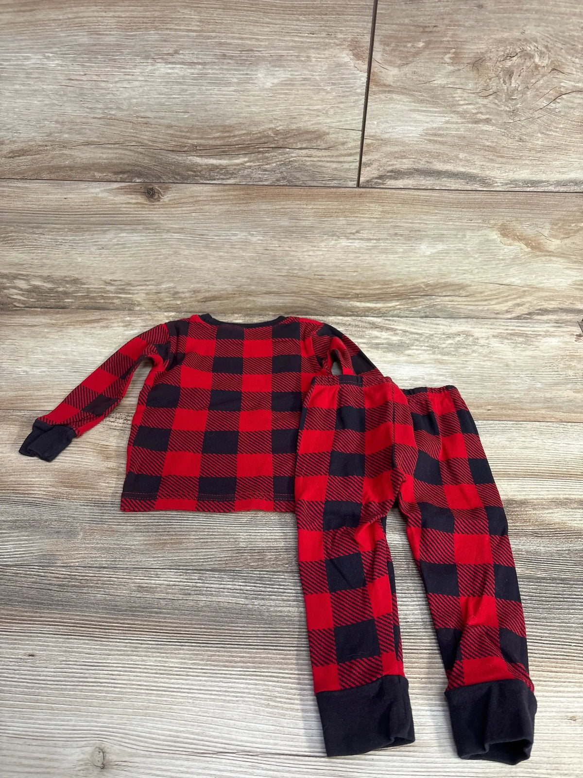 Red and black plaid long sleeve toddler pajama set with black cuffs on wood background