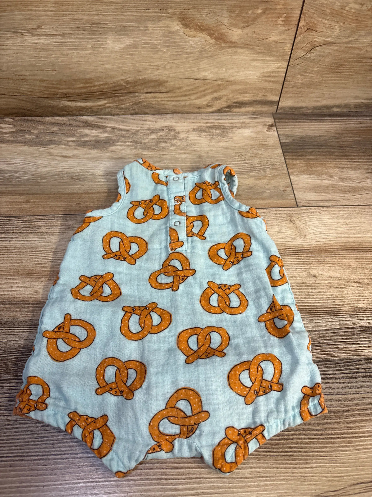 Front view of Old Navy baby gauze tank romper with orange pretzel print and front snaps on wood floor