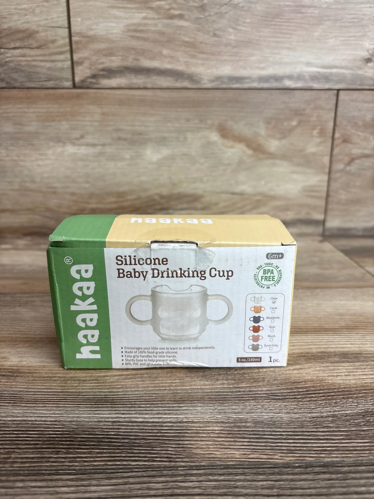 Front of Haakaa silicone baby cup box showing product image, ‘Silicone Baby Drinking Cup’ headline and BPA free badge on wood table