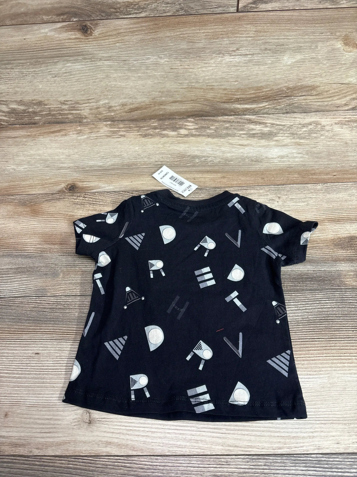 Front view of black Boxlunch x Star Wars baby shirt with allover print of letters spelling Darth Vader on wood plank background