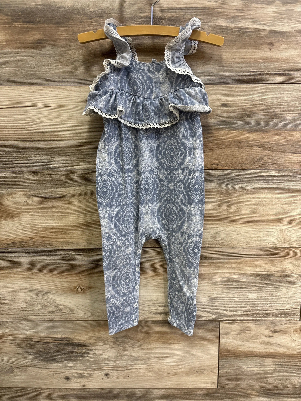 Front view of Jessica Simpson blue floral jumpsuit for 18 months with lace-trimmed ruffles and snap closures on wood