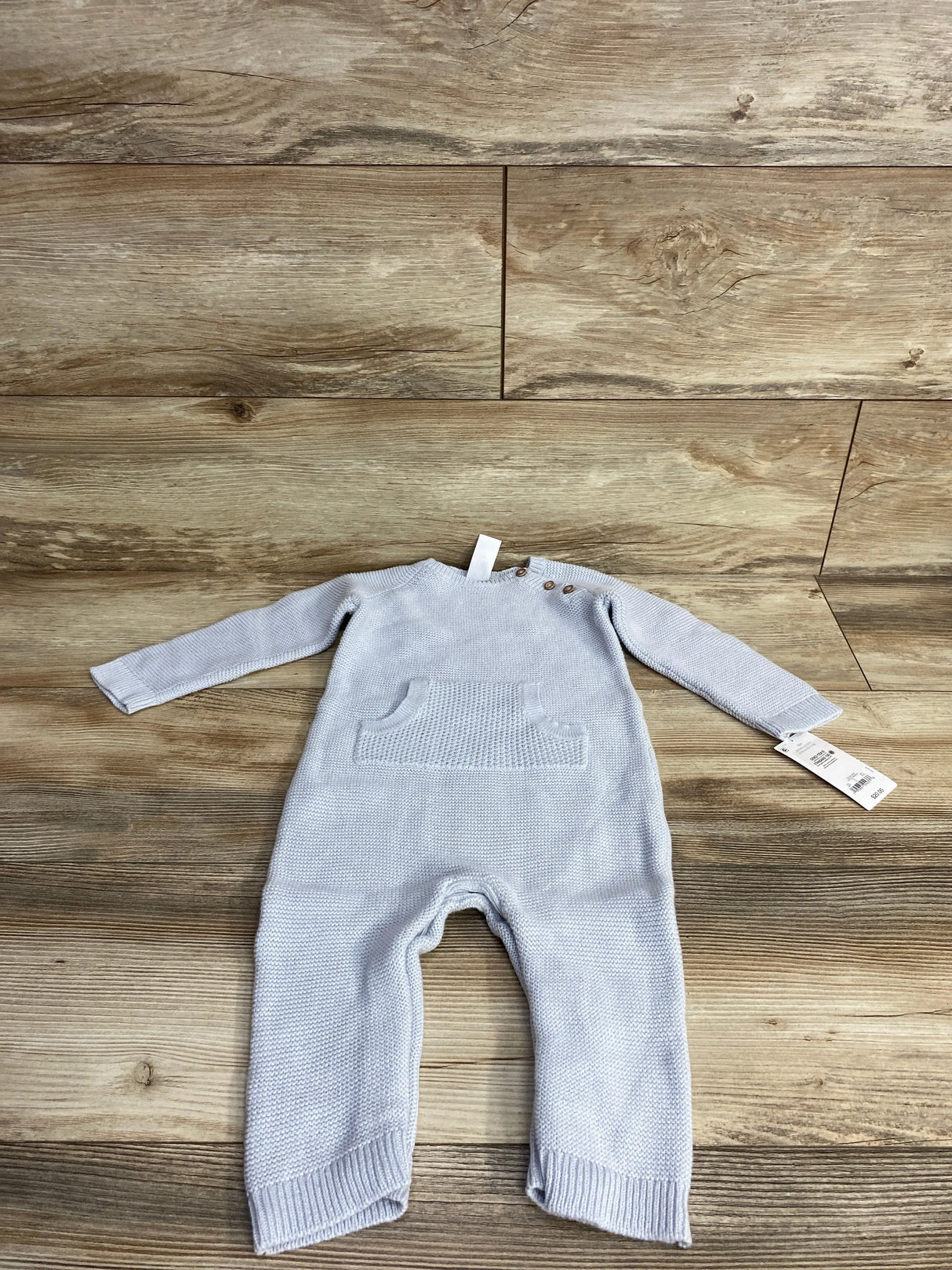 Light blue knitted baby romper with front pocket and wooden buttons on wood background