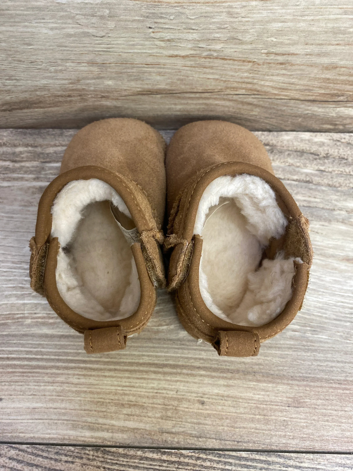 Pair of brown baby moccasin shoes with soft white fleece lining on wooden surface