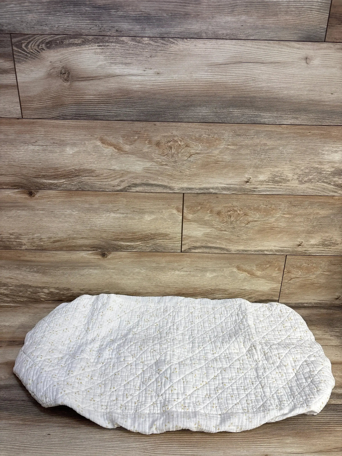 Top view of Crate Kids gauze changing pad cover with quilted diamond stitching and small gold stars on wood background