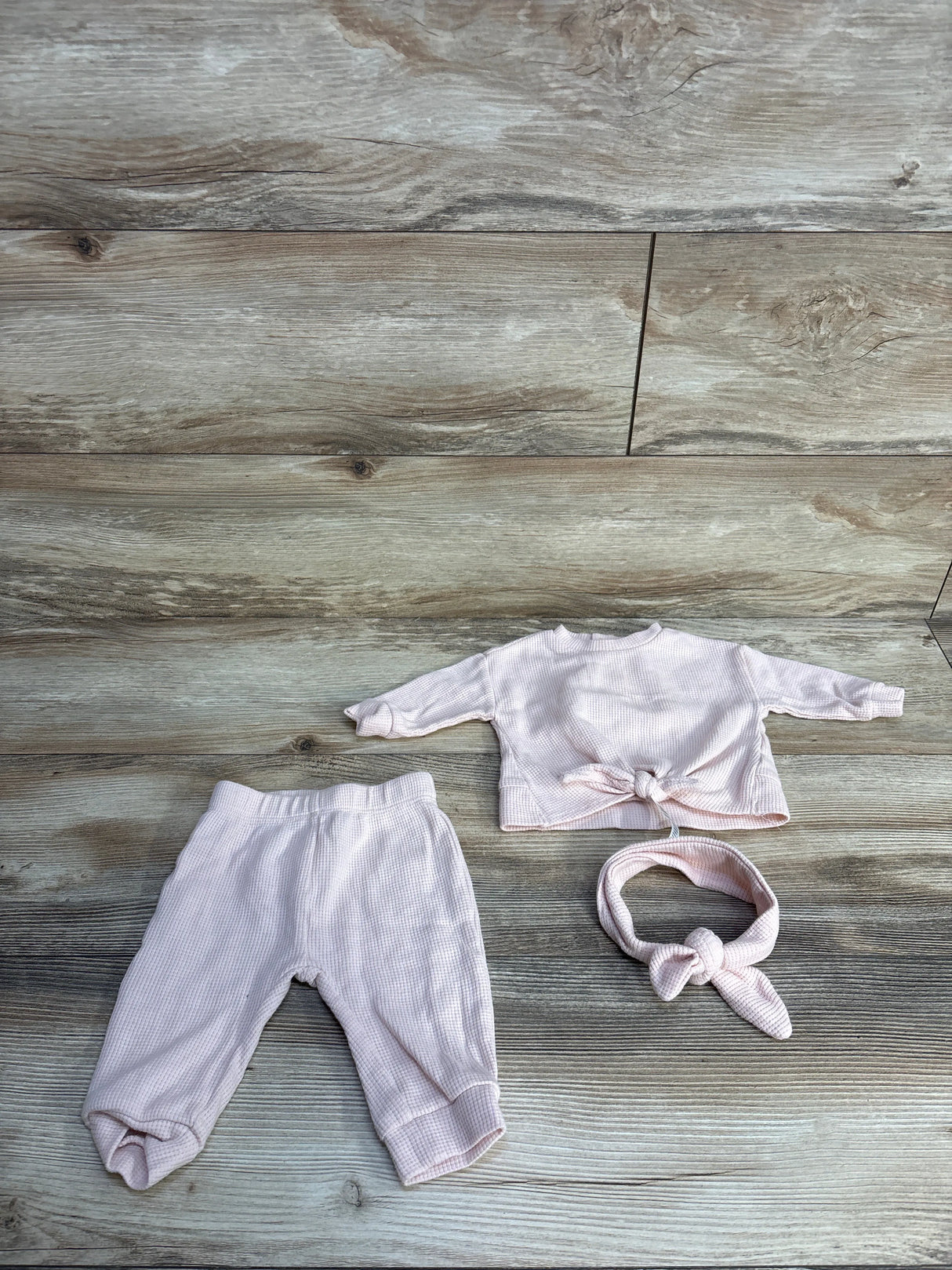 Pink baby outfit set with pants, long-sleeve top, and headband on wooden background
