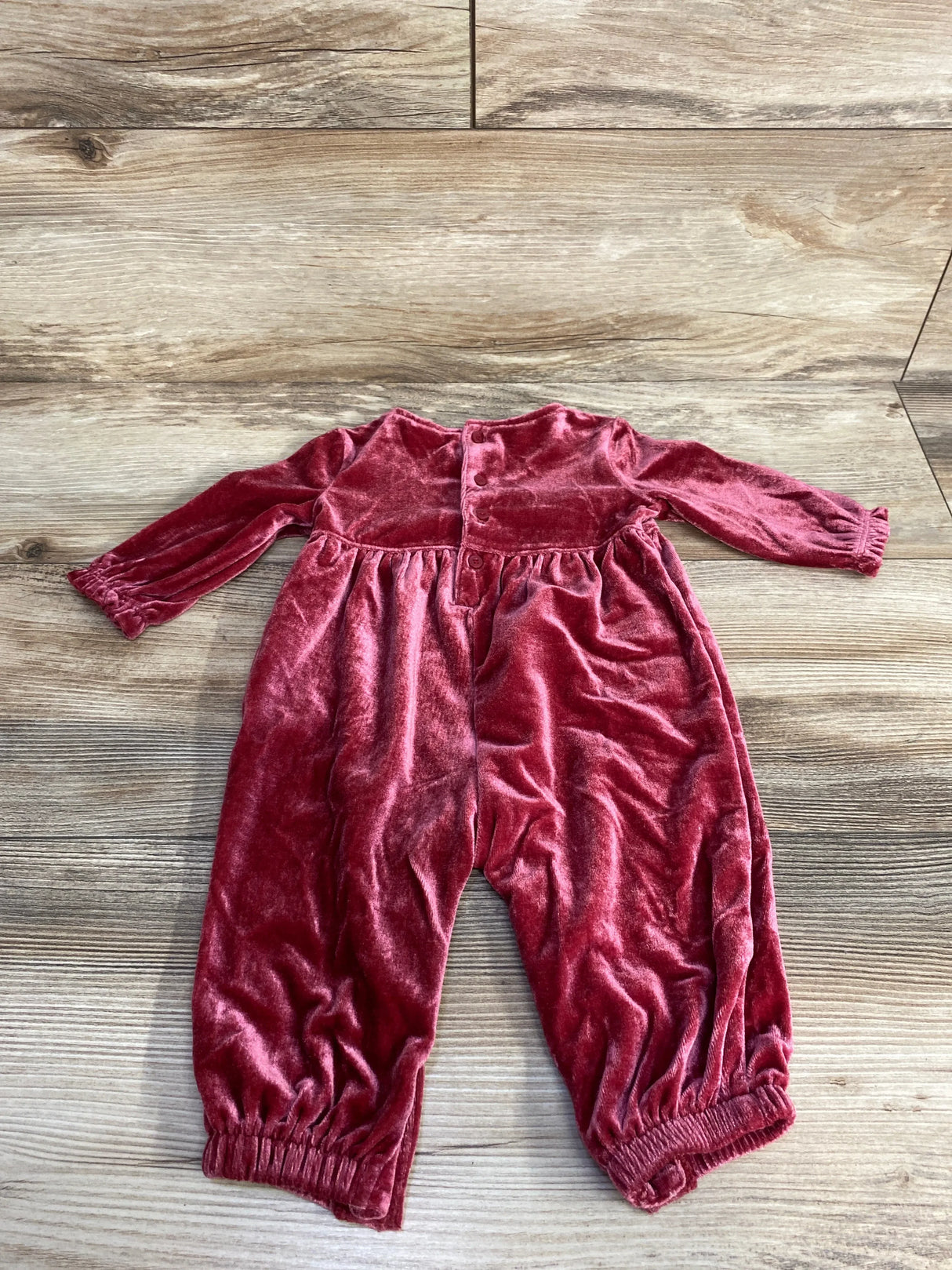 Soft velvet long-sleeve baby jumpsuit in dusty rose on wood floor background