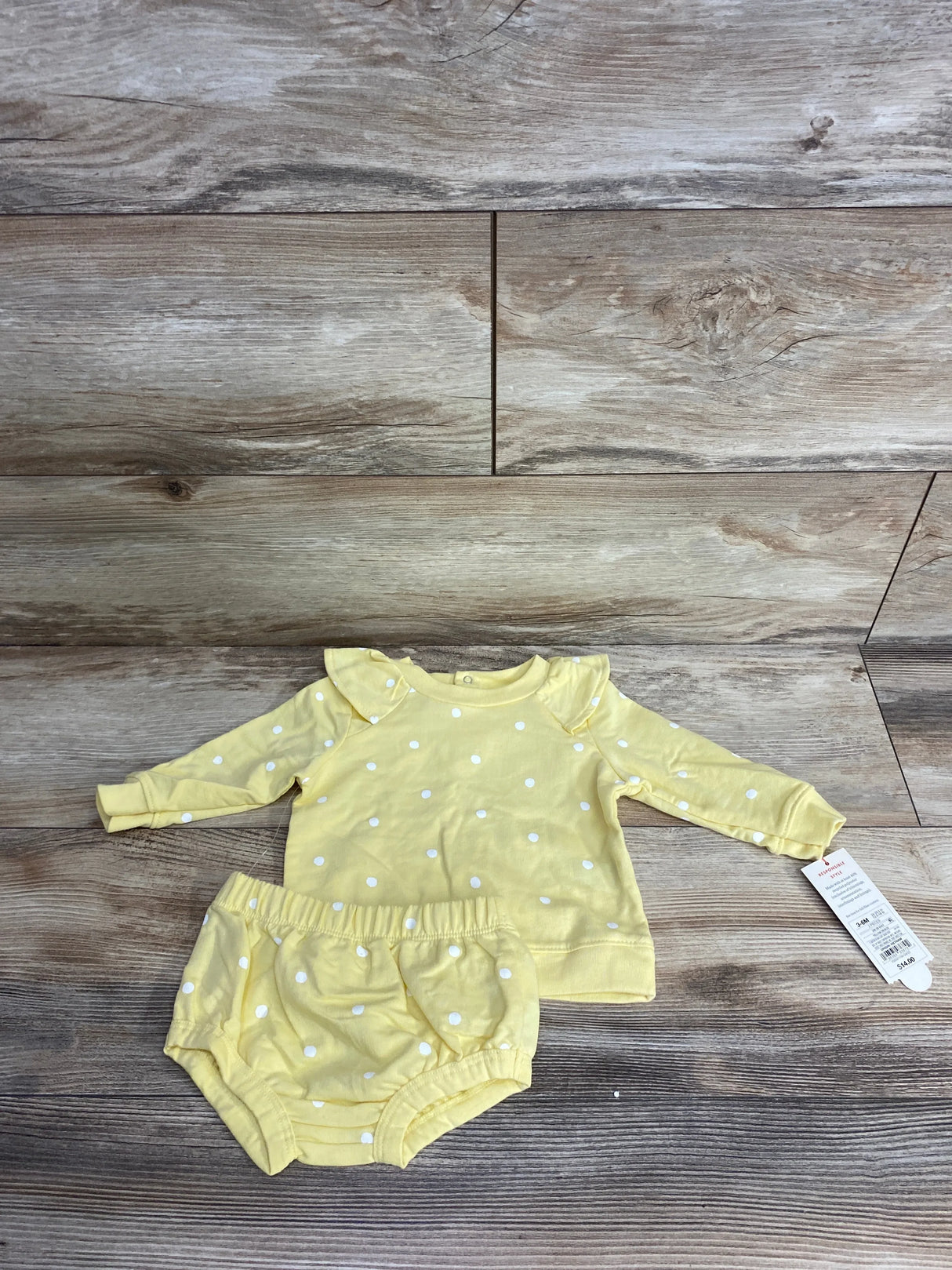 Yellow baby outfit with white polka dots, long sleeve top and bloomers on wood floor