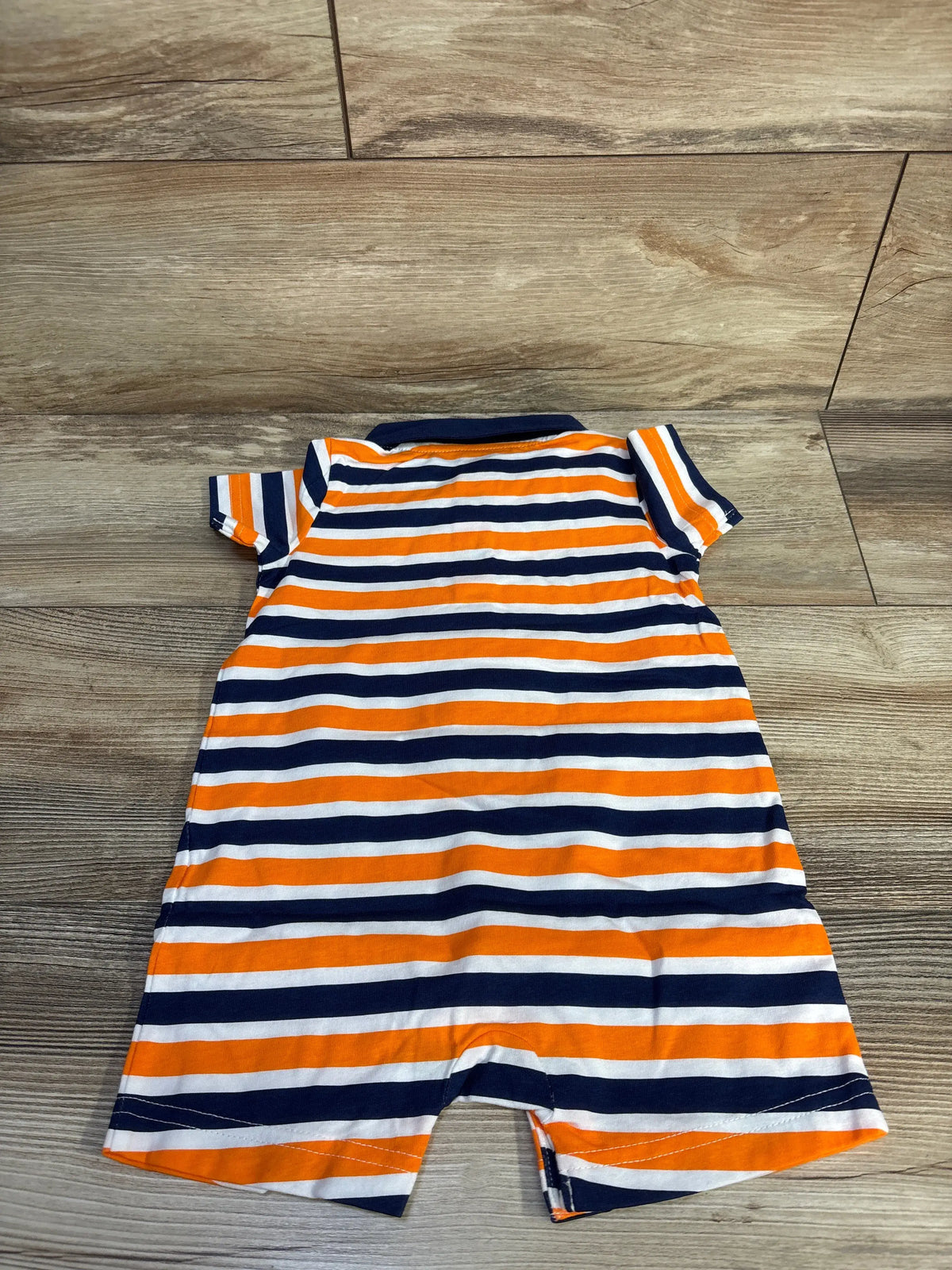 Front view of navy striped polo shortie romper showcasing polo collar and short sleeves on a wood floor