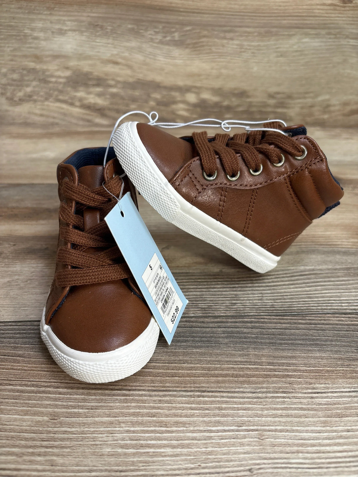 Brown toddler high top sneakers with white soles and price tag on wooden background