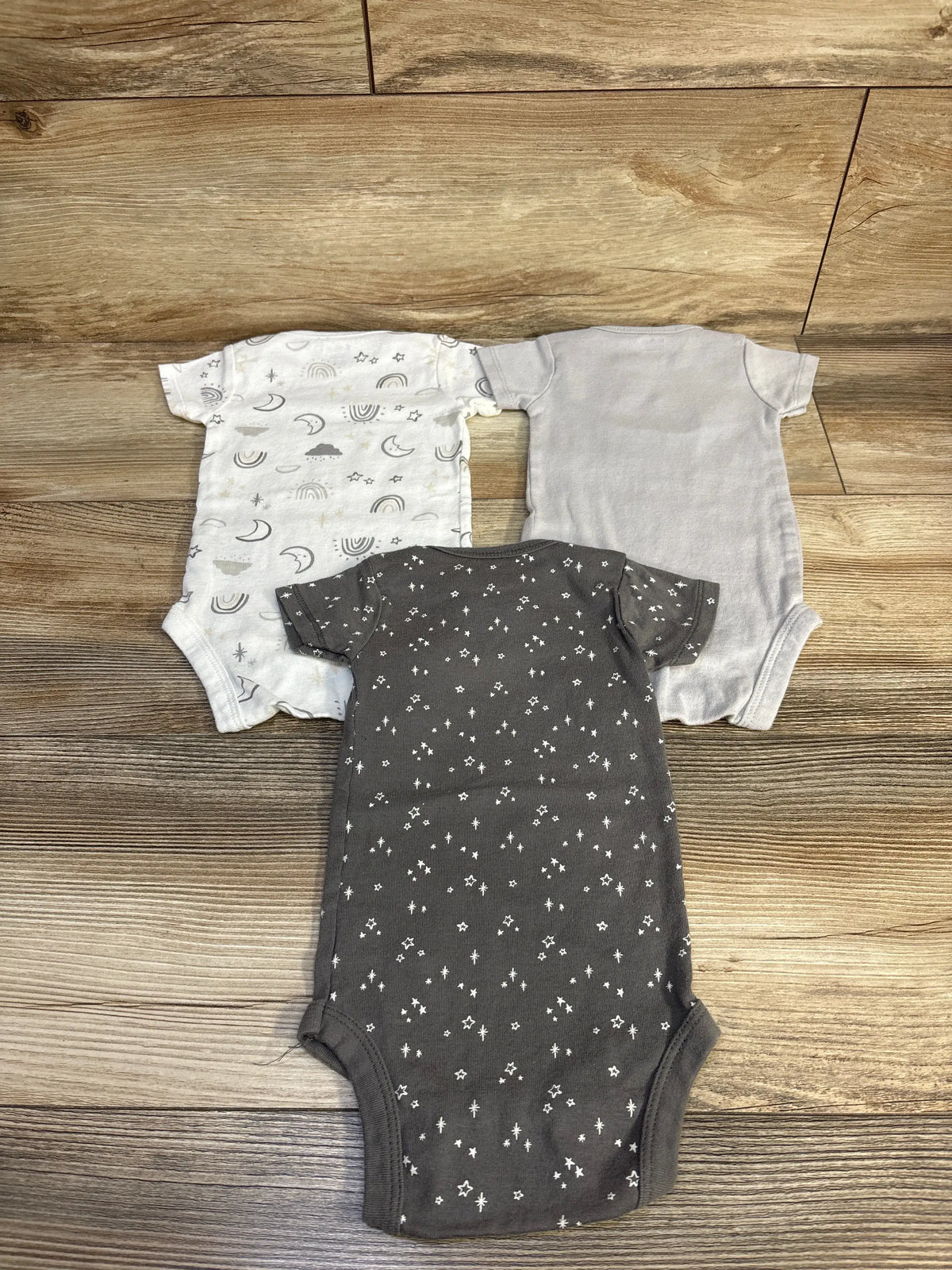 Top view of Gerber three-pack bodysuits showcasing short sleeves and varied grey celestial prints on a wood-grain background
