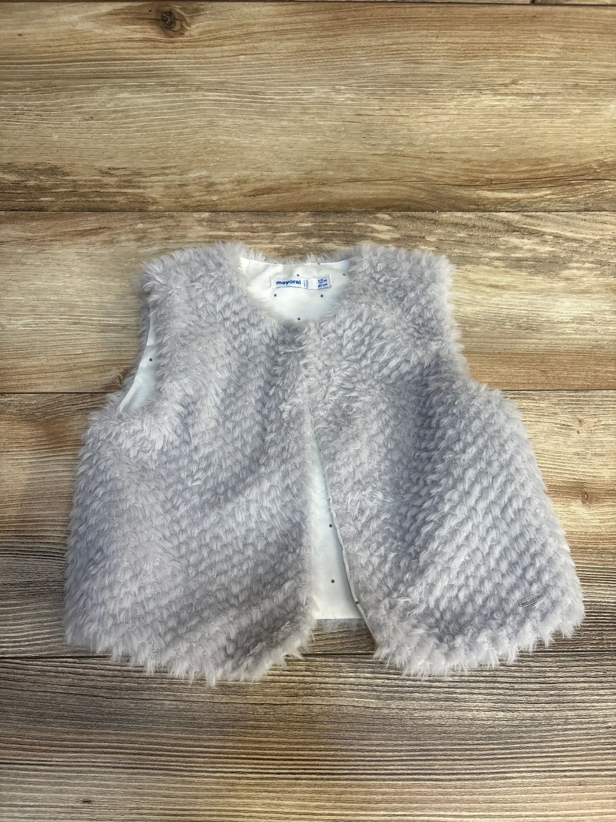 Gray fuzzy baby vest for 12 months, soft faux fur toddler outerwear on wood background