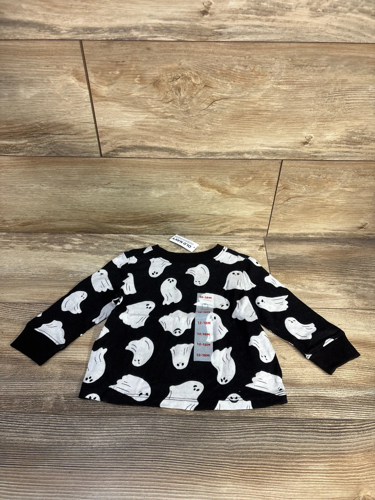 Front view of Old Navy black ghost shirt with white ghost print and long sleeves on a wood background