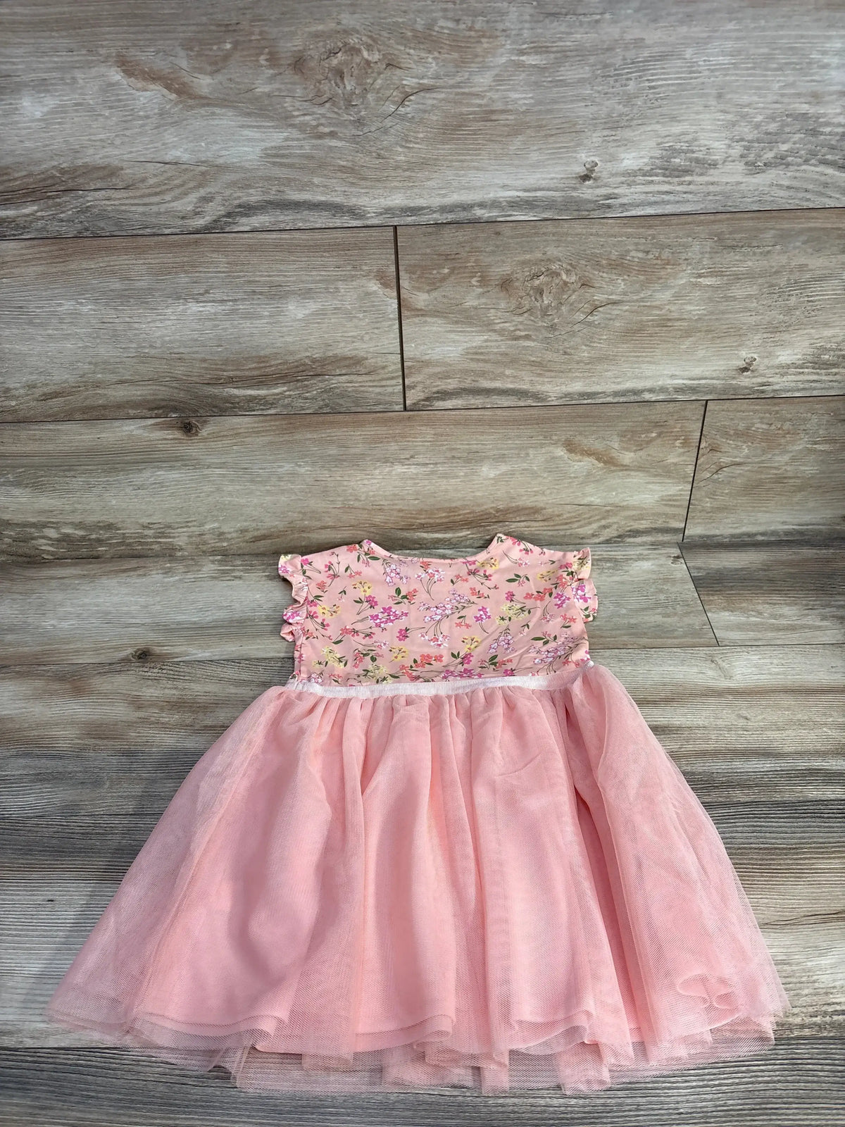 Flat lay of pink Children’s Place girls’ dress showing floral knit bodice, ruffled cap sleeves and tulle skirt on wood background